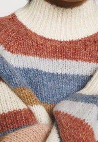 Sweter pleciony z wysokim kołnierzem, w paski w kolorach rdzy, kremowym, jasnoniebieskim i brązowym. Miękki, teksturowany materiał wełniany zapewnia ciepło.