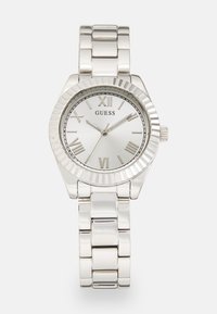 Silver stainless steel wristwatch with a round case, textured bezel, white dial, Roman numerals, and a link bracelet. Brand name "Guess" displayed.
