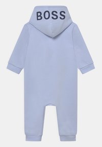 Lichtblauw jumpsuit met capuchon, lange mouwen, elastische manchetten en de tekst "BOSS" in het zwart op de achterkant. Zachte en gladde stoftextuur.
