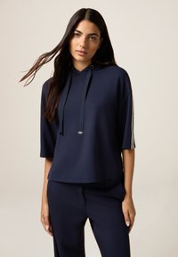 Sudadera con capucha de color azul marino y manga corta, con franjas en contraste en las mangas y un diseño de ajuste relajado. Textura suave.