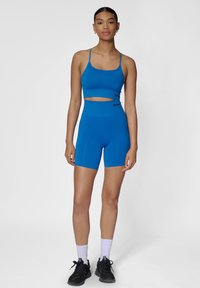 Blauwe sportbeha en set met hoogpants, rekbare stof, fitted ontwerp, cropped top met uitsnijding, gecombineerd met zwarte sneakers.