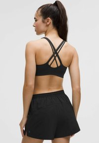Sujetador deportivo negro con un diseño de espalda cruzada, combinado con pantalones cortos deportivos negros que cuentan con una cinturilla elástica y bolsillos.