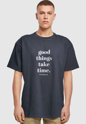 Dark gray oversized cotton t-shirt featuring white text: "good things take time." and the hashtag #TrustTheJourney. Short sleeves, round neckline.