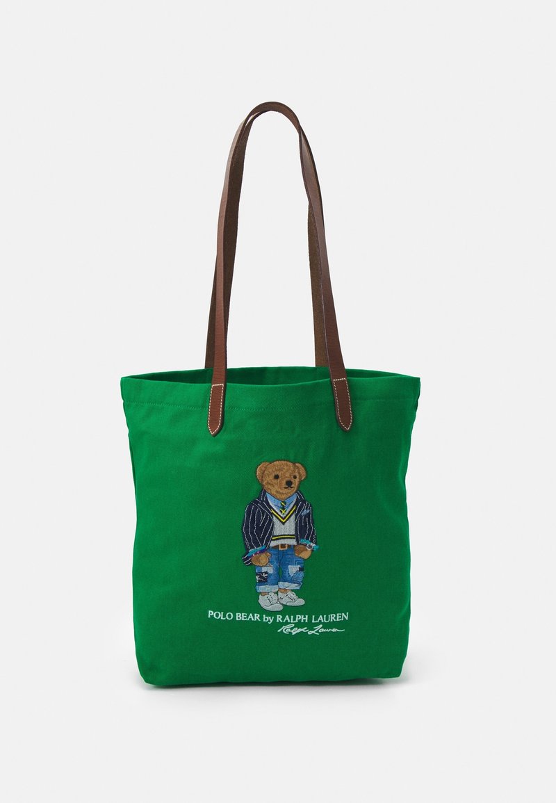 Sac cabas vert avec des anses marron représentant un ours en peluche portant un blazer, un pull, un jean et des baskets, avec le texte « Polo Bear by Ralph Lauren » en dessous.