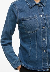 Jeans jakna v temno modri barvi, z dvema žepoma na prsih, gumbi za zapiranje in ovratnikom. Gladka tekstura z oprijetim dizajnom.