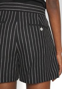 Černobílé pruhované šortky se strukturovanou tkaninou, širokým pasem, dvěma bočními kapsami a knoflíkovým detailem na kapse.