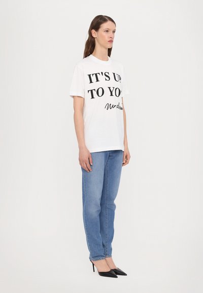 Vit bomullströja med svart text "DET ÄR UPP TILL DIG" och signatur. Matchad med ljusblå denimjeans och svarta spetsiga klackar.