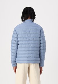 Lyseblå pufferjakke med horisontalt quiltet design, krage og lange ermer. Myk tekstur, minimalistisk stil og lett utseende.