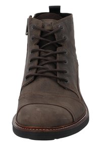 Botín de cuero marrón hasta el tobillo con cordones en la parte frontal y suela de goma. Cuenta con una puntera reforzada y costuras visibles a lo largo de los bordes.