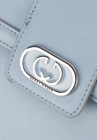 Ljusblå handväska med texturerad yta, förladd med ett silverfärgat lock som har texten "GERRY WEBER", framhäver mjuka kurvor och kanter.