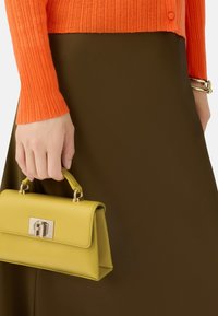 Kleine gele leren handtas met een gestructureerde vorm, draagriem en zilveren hardware, gecombineerd met een oranje ribbeltrui en een bruine rok.