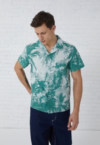Camisa de manga corta en teal y blanco con un patrón de palmeras; cuenta con un cuello de campamento y cierre de botones, hecha de tela ligera.