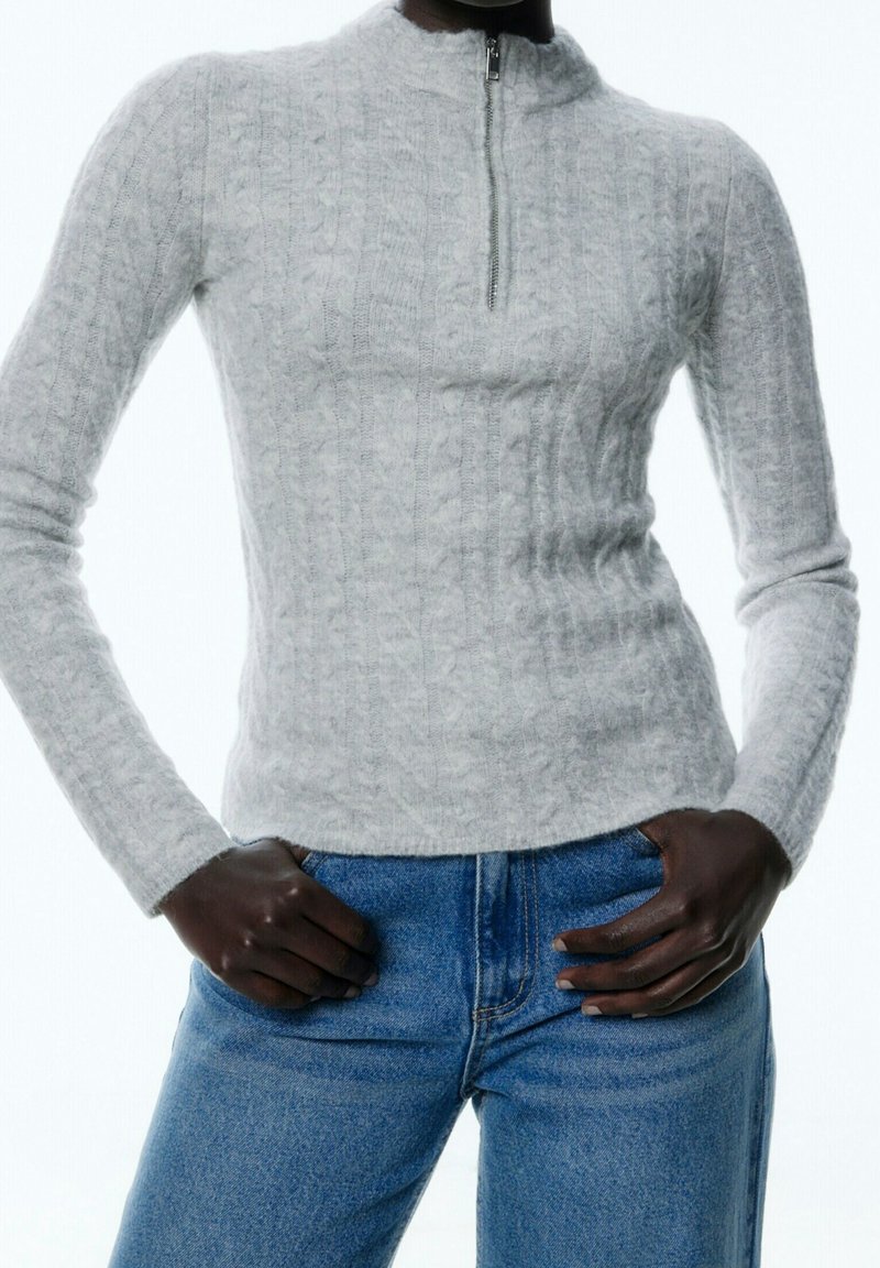 Ljust grå zip-up-tröja med ett texturerat kabelstickat mönster och hög krage, parat med blå denimjeans.