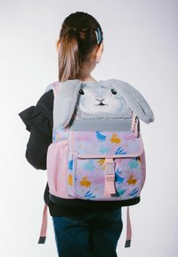 Plecak z jasnoróżowego materiału, z nadrukiem twarzy królika i uszami na górze. Kolorowe wzory królika zdobią całą powierzchnię plecaka, który ma regulowane ramiączka.