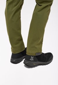 Černé turistické boty z kvalitní nubukové kůže a síťoviny, s texturovanou podrážkou a logem, v kombinaci s olivově zelenými zúženými kalhotami.