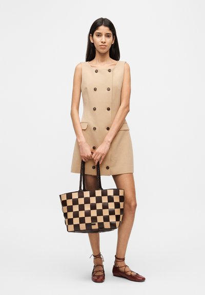Beiges ärmelloses Kleid mit doppelt geknöpften Knöpfen und Seitentaschen; braune und cremefarbene karierte Tragetasche mit geflochtenen Griffen.