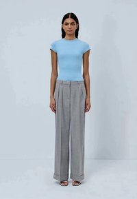 T-shirt ajustado azul claro com mangas curtas, combinado com calças cinzas de xadrez de cintura alta, apresentando pregas e um corte sob medida.