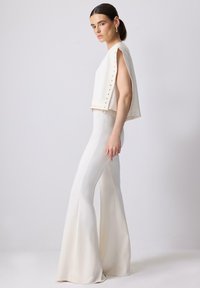 White cropped top with side studs paired with white flared pants. Smooth texture, minimalist design, and tailored fit accentuate elegance.