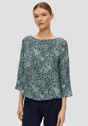 Blouse ample avec une base noire et un motif abstrait vert et blanc. Présente un décolleté large et des manches trois-quarts.