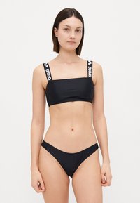 Black bikini set featuring a square-neck bandeau top with logo straps and low-rise bottoms, made from smooth, stretchy fabric.