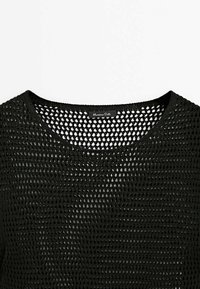 Haut en tricot noir avec un design en mailles larges et ouvertes. Il se distingue par un col rond et un branding minimal au niveau du col.