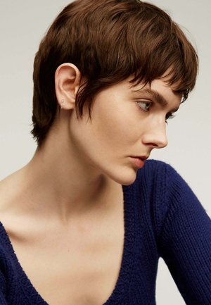 Suéter de punto navy de manga corta y cuello en V profundo con un patrón texturizado. La modelo tiene el cabello corto castaño y lleva un pequeño aro de oro.