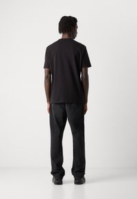 Tricou scurt negru cu guler rotund, asociat cu blugi negri din denim. Materialul pare neted și are o croială lejeră.