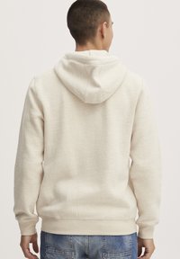 Hettegenser i lys beige, laget av myk bomullsblanding. Har ribbede mansjetter og falmer, med sømdetaljer og en avslappet passform.