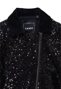 Czarna kurtka bomberka z ozdobami z cekinów, aksamitnym kołnierzem i zapięciem na zamek. Etykiety widoczne wewnątrz kołnierza.