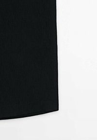Gros plan d'un vêtement en tissu côtelé noir avec un ourlet droit sur fond blanc.