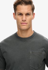 Donkergrijze korte mouwen t-shirt van zachte stof, met een ronde hals en een opgestikte zak met decoratieve stiksels op de borst.