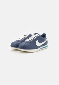 Blue leather sneakers with white accents, lace-up design, and a low profile. Features a blue stripe on the sole and a prominent swoosh logo.