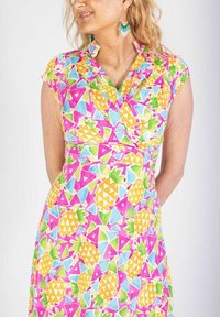 Färggklad klänning med en livlig ananas och geometriskt mönster i nyanser av rosa, gult, grönt och blått med en omslagsstil.