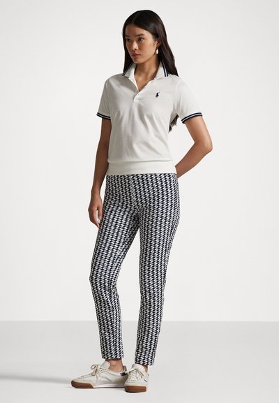 Biele polo tričko s námorníckym lemovaním, spárované s nohavicami v námorníckej a bielej houndstooth vzoru a svetlými teniskami. Jednoduchý, priliehajúci dizajn.