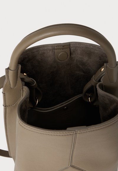 Μπεζ δερμάτινη τσάντα τύπου bucket με στρογγυλές λαβές και σκούρο εσωτερικό από σουέντ, που δείχνει κούμπωμα με κουμπί και εσωτερική τσέπη με χρυσούς κρίκους.
