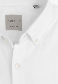 Camisa blanca de botón con un tejido texturizado, cuello clásico y una etiqueta que dice "DAN JOHN REGULAR." Se ven dos botones.