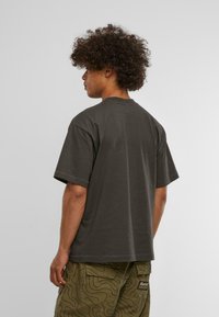 Tamsiai pilkas trumpas rankovėmis marškinėliai, laisvas kirpimas, apvalus iškirpimas, medvilnės medžiaga, matomi iš nugaros, su žalios spalvos krovinių kelnėmis, puoštomis bangų raštu.