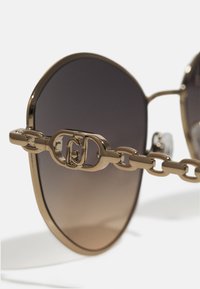 Gold-tone sunglasses with gradient dark lenses. The arms feature a chain link design with a circular logo accent near the hinge.