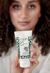 Vit squeeze tube med mun-gel som har grön och svart växtmönster, märkt "teeträdolja," för friska tänder och tandkött.