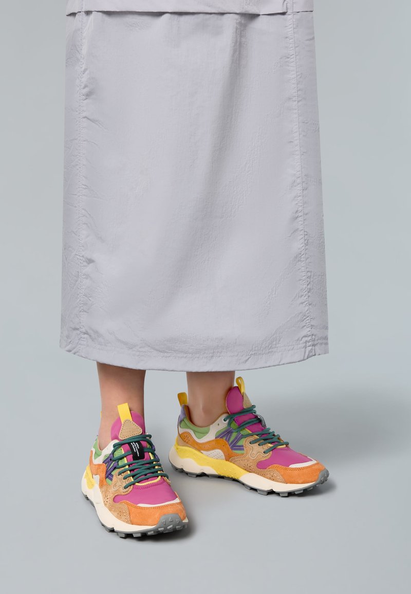 Multicolored sneakers featuring a mix of orange, pink, green, and tan, with a chunky sole and textured materials. Bright laces and accents.
