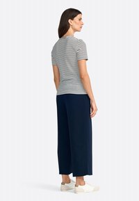 Striped black and white short-sleeve top paired with navy wide-leg pants and white sneakers featuring beige accents. Simple design and relaxed fit.