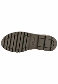 Suela de zapatos de TOMS, de goma texturizada con surcos profundos, en color beige. Logo impreso cerca del centro. Diseño plano y duradero.
