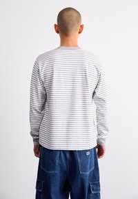 Lys grå langermet skjorte med tynne horisontale hvite striper, ribbet rund hals og tettsittende mansjetter, sammen med mørkeblå cargo-bukser.