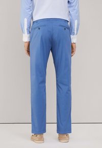 Pantaloni azzurri chiari con vestibilità dritta, due tasche posteriori con chiusure a bottone e una texture in cotone morbido. Indossati con una camicia a righe azzurre chiare.