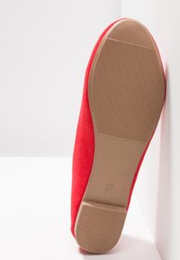 Chaussure plate en suède rouge avec un bout arrondi et une semelle en caoutchouc beige texturée. Taille 37 marquée au fond.