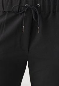 Schwarze Jogginghosen mit einem Kordelzugbund mit metallischen Aglets, weich im Material und mit einem eleganten, glatten Design, ideal für die Freizeit.