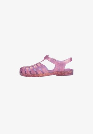 Glittery pink transparent sandal with open sides, slingback design, and a wide strap pattern. Features a sparkly gradient effect.