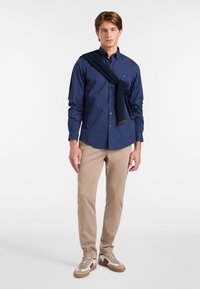 Mornarska majica z dolgimi rokavi in ovratnikom, bež ozke hlače in smetano bele superge s rjavimi detajli. Pulover ovit čez ramena.