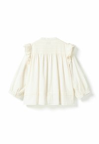Blouse à manches longues couleur crème avec des volants sur les coutures d'épaule et un dos ample froncé, présentée sur fond blanc.