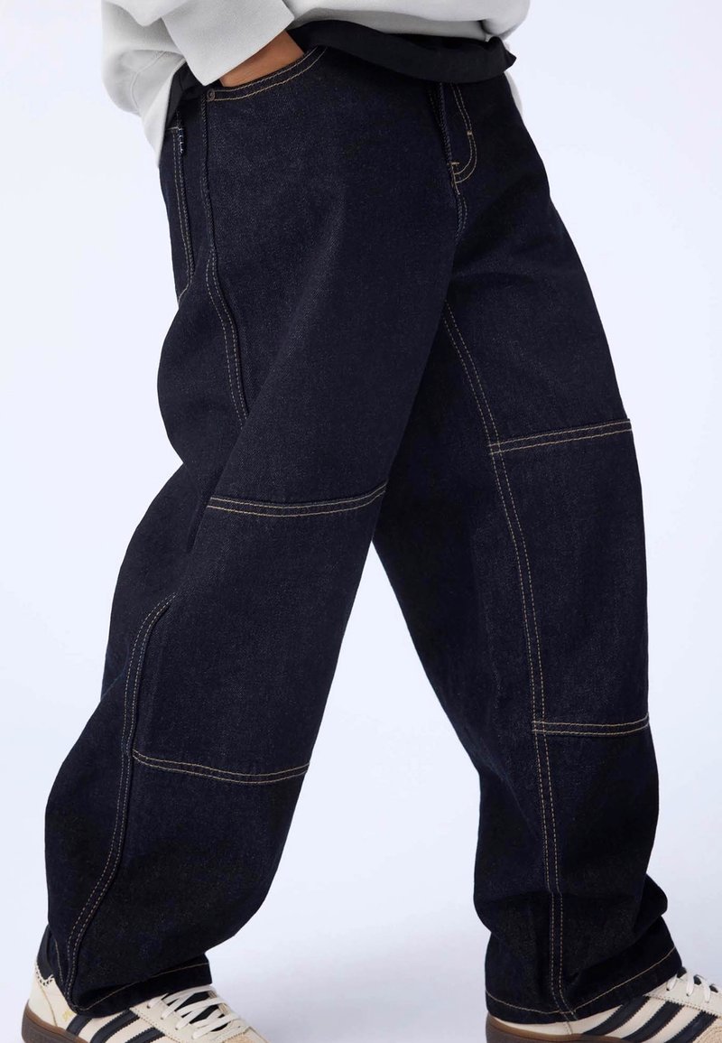 Dark blue denim cargo pants featuring visible stitching, loose fit, side pockets, and a slightly tapered leg. Designed for casual wear.
